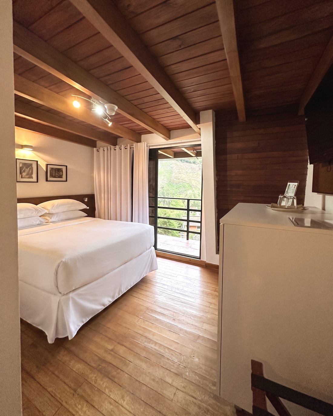 Habitación con techo de madera, cama vestida en blanco y salida al balcón